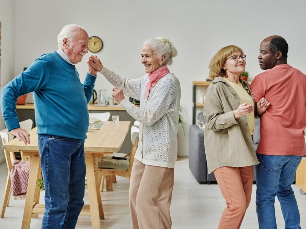 Group of happy elderly people dancing together at party in nursing home