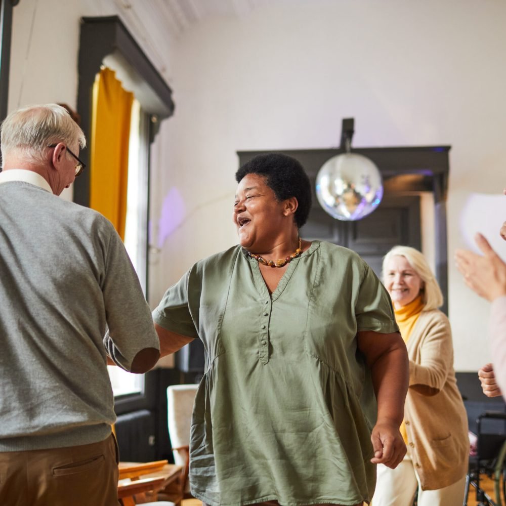 Diverse group of smiling senior people dancing while enjoying activities in retirement home, copy space